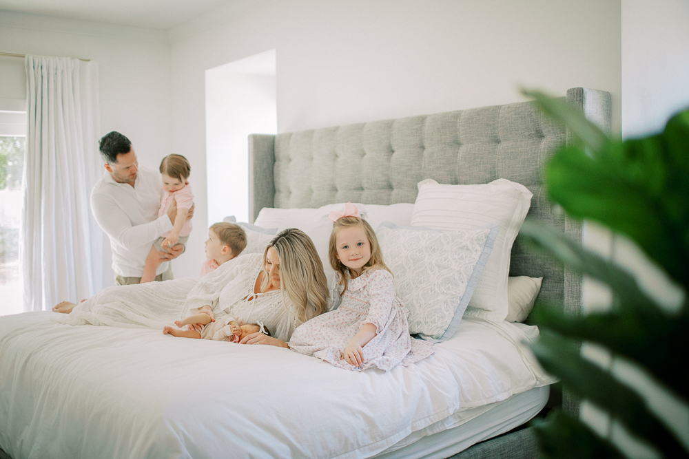 Family sits on bed cuddling newborn baby during in-home Orlando session, showing intimate family connection