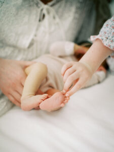 Close-up detail of newborn feet held in sister’s hands during lifestyle photography session in Orlando