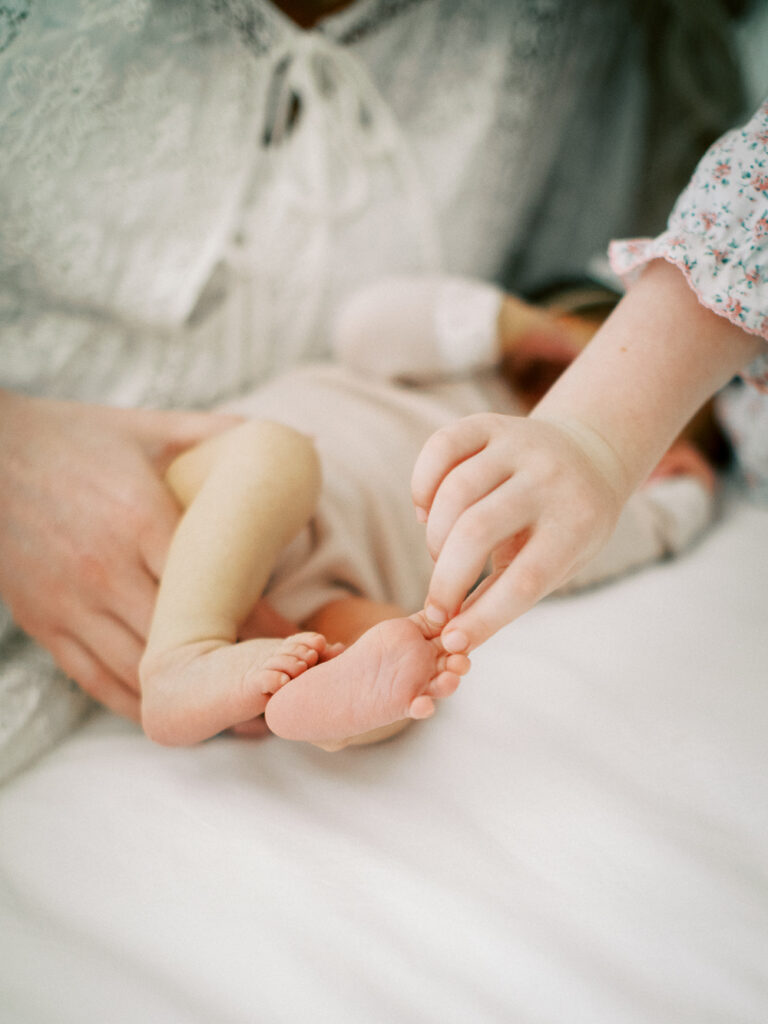 Close-up detail of newborn feet held in sister’s hands during lifestyle photography session in Orlando