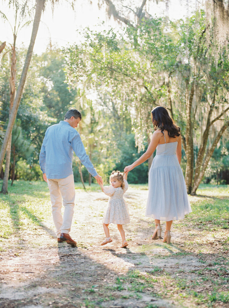Family walking hand in hand through a grassy field at dawn.