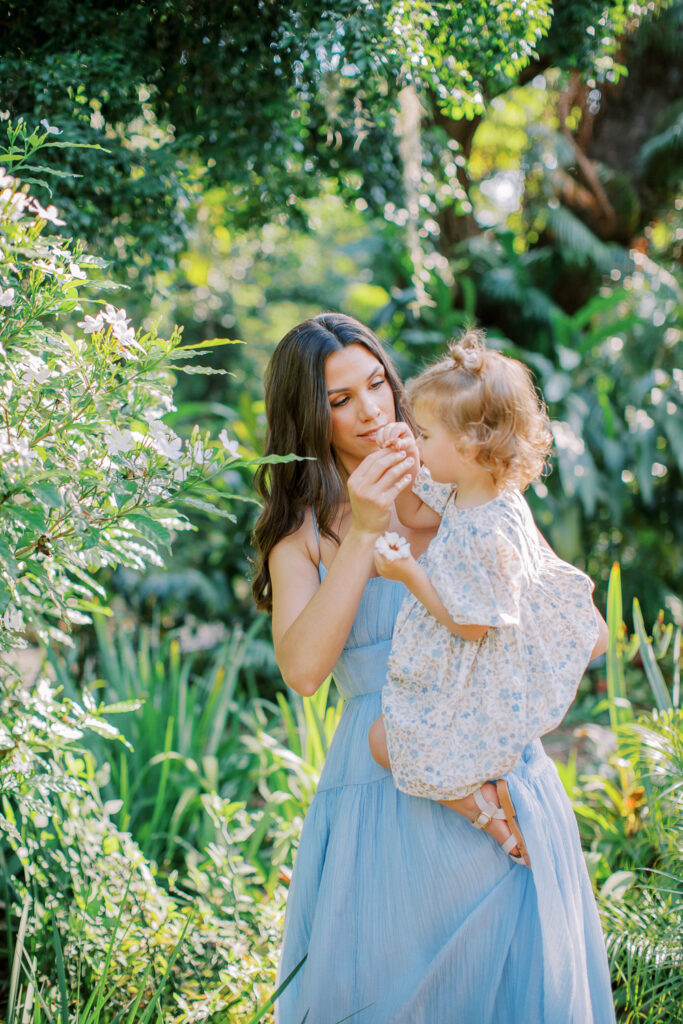 Mom holding toddler to see the flowers during morning portrait session by Orlando family photographer.