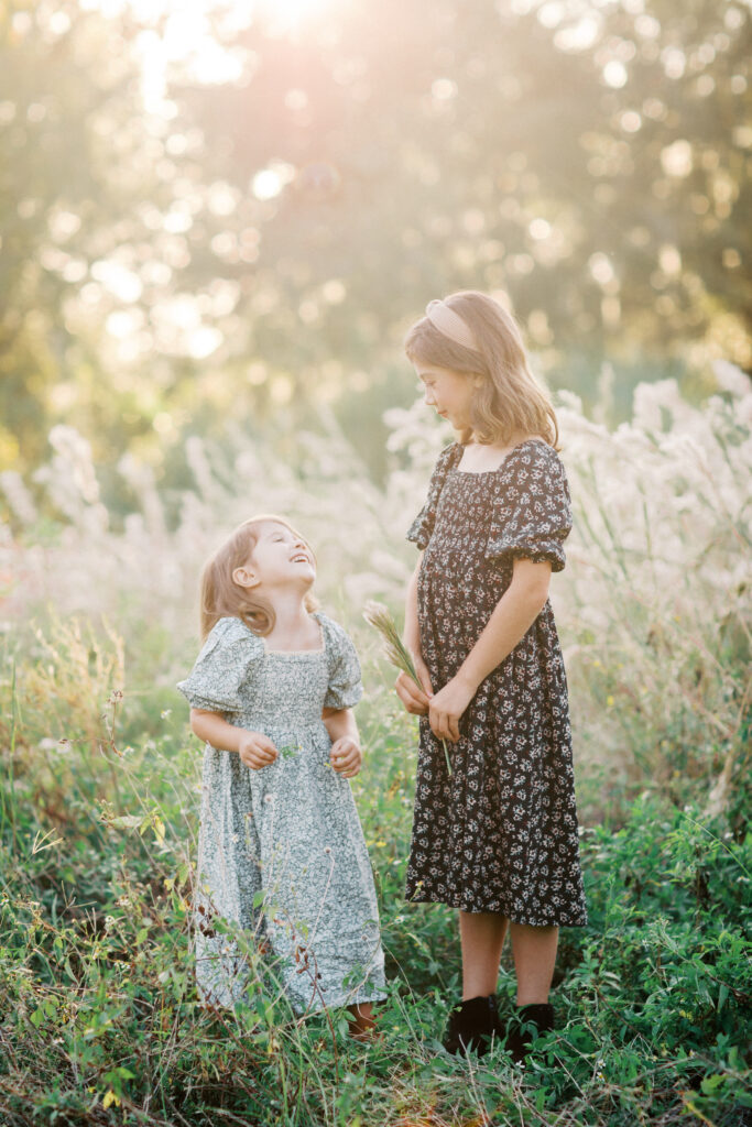 Sisters in a beautiful sun filled field at sunset by Orlando family photographer.